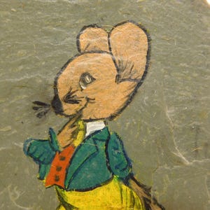 May include: A hand-painted illustration of a mouse wearing a green jacket, orange vest, and yellow pants. The mouse is painted on a gray stone surface. The mouse has brown fur and a black nose and whiskers.