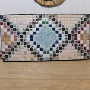 May include: Rectangular mosaic tray with a geometric design. The tray features a central diamond pattern in light blue, surrounded by squares in various colors including beige, white, black, and red. It has black metal handles.