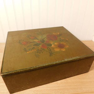 May include: A rectangular wooden box with a hinged lid. The lid is painted with a floral design featuring red, yellow, and green flowers. The box has a distressed, aged appearance, with a dark brown base and a green-toned lid.