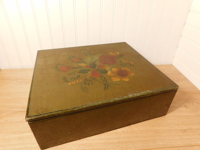 May include: A rectangular wooden box with a hinged lid. The lid is painted with a floral design featuring red, yellow, and green flowers. The box has a distressed, aged appearance, with a dark brown base and a green-toned lid.