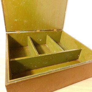 May include: Open wooden box with a hinged lid, painted in shades of olive green and brown. The interior is divided into three compartments. The box appears to be vintage or antique, with visible wear and tear on the paint.