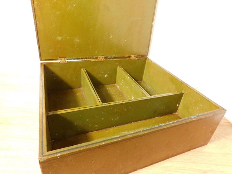 May include: Open wooden box with a hinged lid, painted in shades of olive green and brown. The interior is divided into three compartments. The box appears to be vintage or antique, with visible wear and tear on the paint.