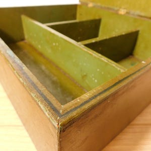 May include: An open, antique wooden box with a brown exterior and a green interior. The box is divided into several compartments. The edges of the box are lined with a dark trim.