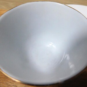 May include: A small, light gray bowl with a gold rim. The bowl is empty and appears to be made of ceramic. The bowl is sitting on a wooden surface.
