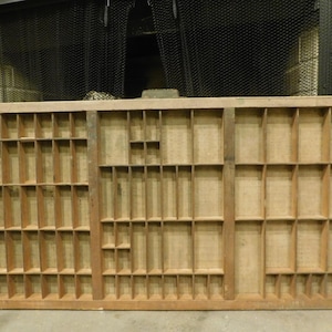 May include: A rectangular wooden printer's tray, featuring a multitude of small, individual compartments. The tray is constructed from light-toned wood, with a grid pattern formed by vertical and horizontal dividers, creating various sized spaces.
