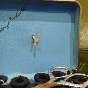 May include: Vintage sewing kit box with a light blue interior. The box contains spools of thread, scissors, and the text "Belding Corticelli" in green script. The box is open, revealing the contents.