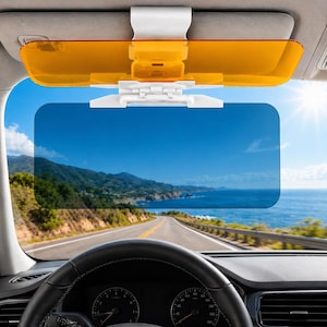 Pode incluir: Para-sol de carro com suporte de montagem branco e dois painéis coloridos. O painel superior é âmbar e o inferior azul, para reduzir o brilho. Vê-se uma estrada costeira e céu azul através do painel inferior.
