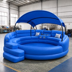 Puede incluir: Un gran salón inflable azul de forma circular con un toldo a juego, escalones integrados y una zona de asientos central. La estructura cuenta con una consola con dos altavoces y dos pequeños cojines cuadrados de color gris claro.