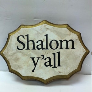 May include: A wooden sign with a gold border and a white background. The sign says "Shalom y'all" in black lettering.