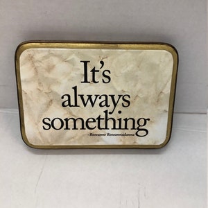 May include: A rectangular sign with a gold border and a white background with a marble-like texture. The sign has black text that reads "It's always something -Roseanne Roseannadanna".
