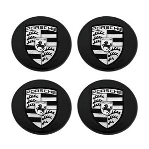May include: Four black Porsche wheel center caps. Each cap features the Porsche logo in white and black, including the word "PORSCHE" at the top and "STUTTGART" below the logo. The logo is a shield with a horse in the center.
