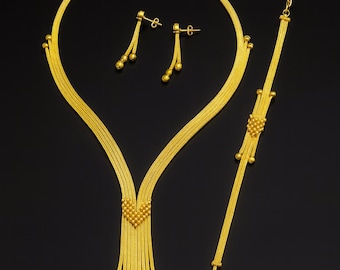 May include: A complete gold jewelry set, including a necklace, earrings, and bracelet, displayed against a black background. The necklace features a heart-shaped pendant with dangling strands and beaded accents. The earrings are drop style, and the bracelet has a similar design.