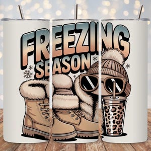 Puede incluir: Un vaso blanco con temática invernal. El diseño presenta las palabras "FREEZING SEASON" en una fuente degradada, junto con ilustraciones de botas de invierno, un gorro, gafas de sol y una taza con estampado de leopardo. El vaso tiene una pajita.