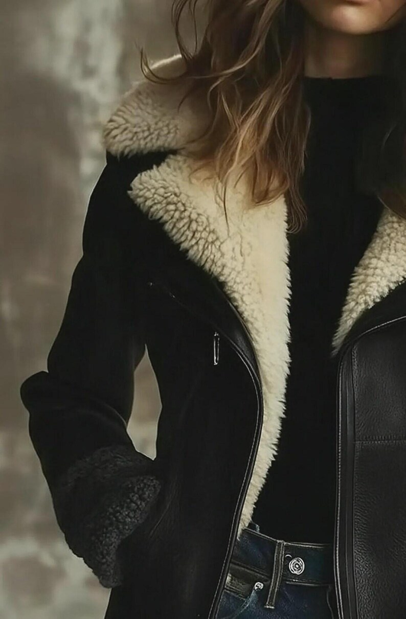 Peut inclure: Veste en cuir noir avec une doublure en peau de mouton cr&egrave;me autour du col et des poignets. La veste a une fermeture &eacute;clair et un style motard classique. Le mod&egrave;le porte un col roul&eacute; noir et un jean bleu.