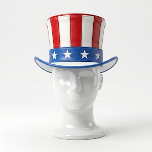 May include: A patriotic Uncle Sam hat with red and white stripes and a blue band with white stars. The hat has a blue brim and is displayed on a white mannequin head. Perfect for Independence Day or patriotic events.