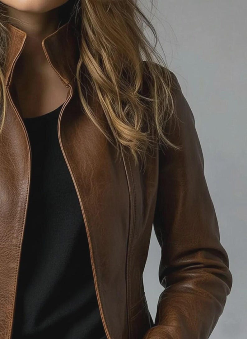May include: A brown leather jacket with a high collar. The jacket is a medium brown color and has a tailored fit. The sleeves are long and the jacket appears to be made of a soft leather material.