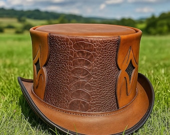 May include: A brown leather top hat with a wide brim, featuring a textured, dark brown center panel and decorative side accents. The hat is set against a backdrop of green grass and a blue sky, showcasing its craftsmanship.