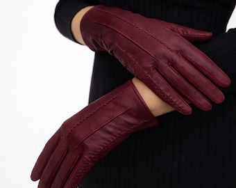 Peut inclure: Gants en cuir bordeaux avec une bordure festonnée. Les gants sont d'un rouge profond et semblent être en cuir souple. Le texte "studioOFleather" est visible dans le coin supérieur gauche.