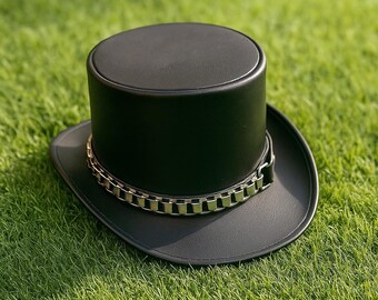 May include: A black top hat with a silver chain band, resting on a bed of green grass. The hat has a cylindrical crown and a wide brim. The chain band adds a decorative touch to the classic design.