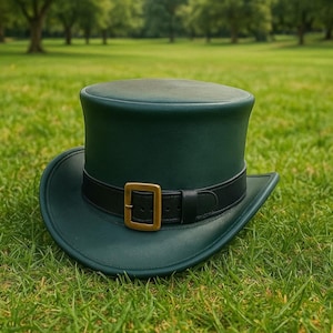 May include: A dark green top hat with a black band and a gold-colored buckle. The hat is sitting on a bed of green grass, with a blurred background of trees and a grassy field.