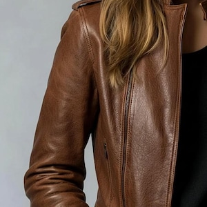 May include: A brown leather jacket with a zip-up front and a classic collar. The jacket has a textured appearance and a tailored fit. The sleeves are long, and the jacket appears to be made of high-quality leather.