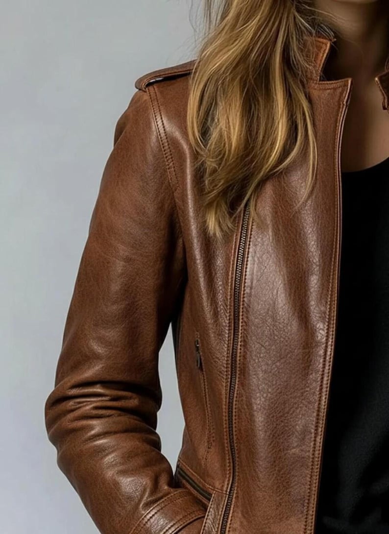 May include: A brown leather jacket with a zip-up front and a classic collar. The jacket has a textured appearance and a tailored fit. The sleeves are long, and the jacket appears to be made of high-quality leather.