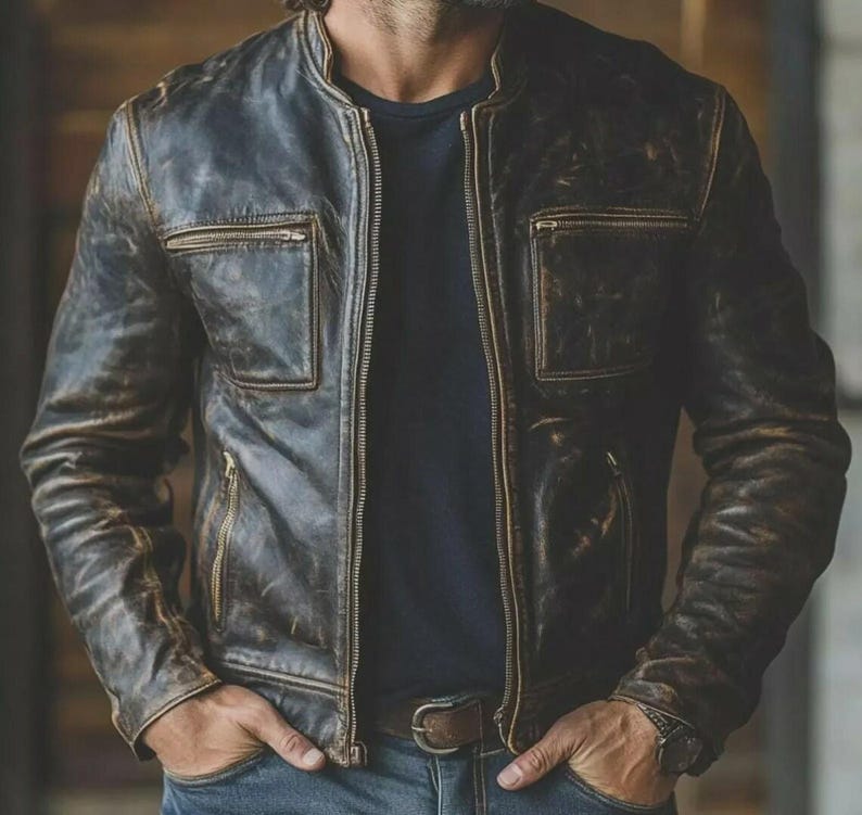 May include: A distressed brown leather jacket with a zip-up front, two chest pockets, and a stand-up collar. The jacket has a worn, vintage look with visible texture and a dark blue lining. The jacket is worn with a dark blue shirt and blue jeans.