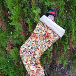 May include: A Christmas stocking with a white faux fur cuff and a colorful pattern of cats, dogs, and floral elements. A snowman with a black top hat and red scarf peeks out from behind the stocking, which is hanging on a green bush.