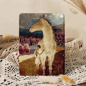 May include: Rectangular art print featuring a beige horse with a child embracing it. The artwork has a muted color palette with shades of brown, blue, and red. The background depicts a landscape with trees and flowers.