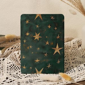 Op de afbeelding: Een rechthoekig, donkergroen decoratief item met een gouden sterrenpatroon. De sterren variëren in grootte en zijn verspreid over het oppervlak. Het item wordt weergegeven op een wit kanten tafelkleed.