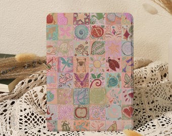 May include: A colorful, square-patterned notebook featuring a variety of whimsical illustrations. The design includes images of fruits, insects, and hearts in a patchwork style. The notebook is displayed on a white lace tablecloth.