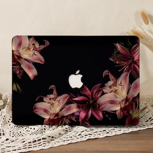 May include: A black laptop cover featuring a vibrant floral print of pink and deep red lilies. The design showcases multiple lily blossoms arranged around the centre, where a white Apple logo is clearly visible against the dark background.