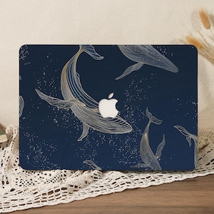 Puede incluir: Una funda para portátil de color azul marino oscuro con un patrón repetitivo de ballenas dibujadas con líneas doradas que nadan entre motas blancas dispersas. El diseño incorpora el recorte central del logotipo de Apple.