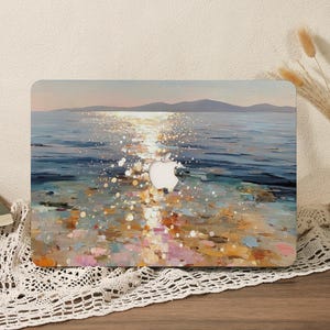 May include: A laptop case with an impressionistic seascape painting. The design shows a sunlit ocean and distant mountains. The Apple logo is in the centre of the case.