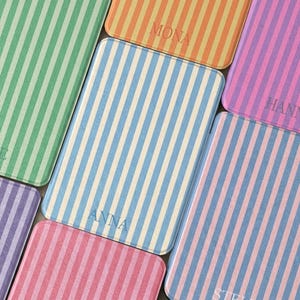 May include: A selection of rectangular cases featuring vertical stripes in pastel shades of green, orange, blue, pink, and purple. Some cases are inscribed with names like "ANNA" and "MONA".