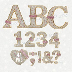 May include: Gold-toned alphabet letters, numbers, and symbols encrusted with white and pink gemstones. The letters A, B, and C, numbers 1, 2, 3, and 4, and symbols including a heart, comma, exclamation point, ampersand, and question mark are displayed.