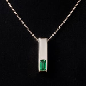 May include: A silver-toned necklace featuring a vertical rectangular pendant. The pendant has a smooth, opaque white upper section and a vibrant, rectangular green gemstone set at the base. The piece hangs from a delicate, thin silver-toned chain.