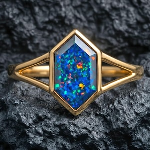 May include: A gold ring featuring a hexagonal, iridescent blue opal gemstone. The opal displays a vibrant array of colors, including green, orange, and yellow. The ring's band is a simple, polished gold design.
