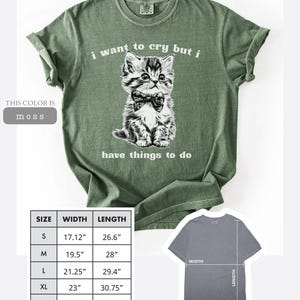 May include: Moss green t-shirt with a graphic of a kitten wearing a bow tie, and the text "i want to cry but i have things to do". The shirt sizes range from S (17.12" width, 26.6" length) to 2XL (25" width, 31.6" length).