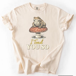 May include: Ivory t-shirt with a detailed illustration of a toad on a red and white mushroom. The text "I Toad YOU SO" is printed below the graphic. The shirt has a classic crew neck and short sleeves.