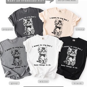 May include: Five t-shirts in various colors: pepper, ivory, grey, white, and black. Each shirt features a graphic of a kitten wearing a bow tie, with the text "i want to cry but i have things to do". The shirts are soft-washed and comfy.