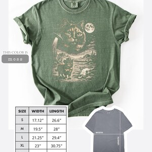 Pu&ograve; includere: T-shirt verde muschio con grafica di un gatto, un UFO, un paesaggio desertico e una luna. La maglietta ha maniche arrotolate e girocollo. Taglie dalla S (43,5 cm di larghezza, 67,6 cm di lunghezza) alla 2XL (63,5 cm di larghezza, 80,3 cm di lunghezza).