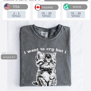 May include: Pepper-colored t-shirt featuring a detailed illustration of a kitten wearing a bow tie, with the text "i want to cry but i" above the image. The shirt is folded and displayed on a white surface.