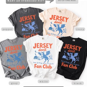 May include: A collection of soft-washed t-shirts in various colors, including pepper, ivory, grey, white, and black. Each shirt features the text "JERSEY devil" with a graphic of a mythical creature and the words "Fan Club".