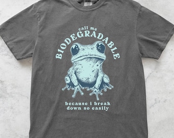 Może przedstawiać: Ciemnoszara koszulka z jasnoniebieską grafiką żaby i napisami "call me BIODEGRADABLE" nad żabą oraz "because i break down so easily" poniżej. Koszulka ma okrągły dekolt.