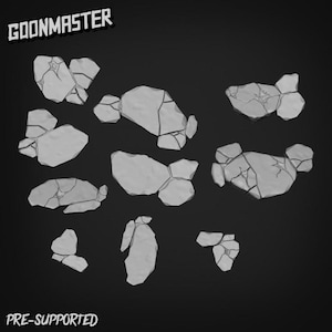 May include: A selection of grey, cracked stone terrain pieces for tabletop gaming. The pieces are of various sizes and shapes, with visible cracks and textures. The image includes the text "GOONMASTER" and "PRE-SUPPORTED".
