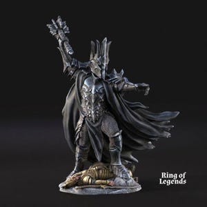 May include: A detailed figurine of a dark armored figure with a raised weapon, standing over a fallen warrior. The figure wears a helmet and cape, with intricate armour details. The base is a stone-like texture, and the overall colour scheme is dark grey.