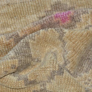 Puede incluir: Primer plano de una alfombra beige texturizada con un patr&oacute;n geom&eacute;trico en tonos marr&oacute;n y gris. Una peque&ntilde;a mancha rosa es visible en la superficie. La alfombra parece suave y afelpada.