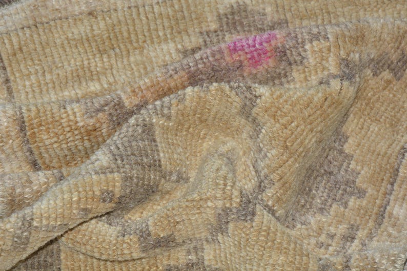 Puede incluir: Primer plano de una alfombra beige texturizada con un patr&oacute;n geom&eacute;trico en tonos marr&oacute;n y gris. Una peque&ntilde;a mancha rosa es visible en la superficie. La alfombra parece suave y afelpada.