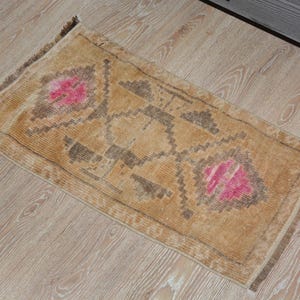 Puede incluir: Una alfombra rectangular de estilo vintage, en tonos beige y marr&oacute;n. La alfombra presenta un dise&ntilde;o central con elementos florales rosas y patrones geom&eacute;tricos. Est&aacute; colocada sobre un suelo de madera clara.